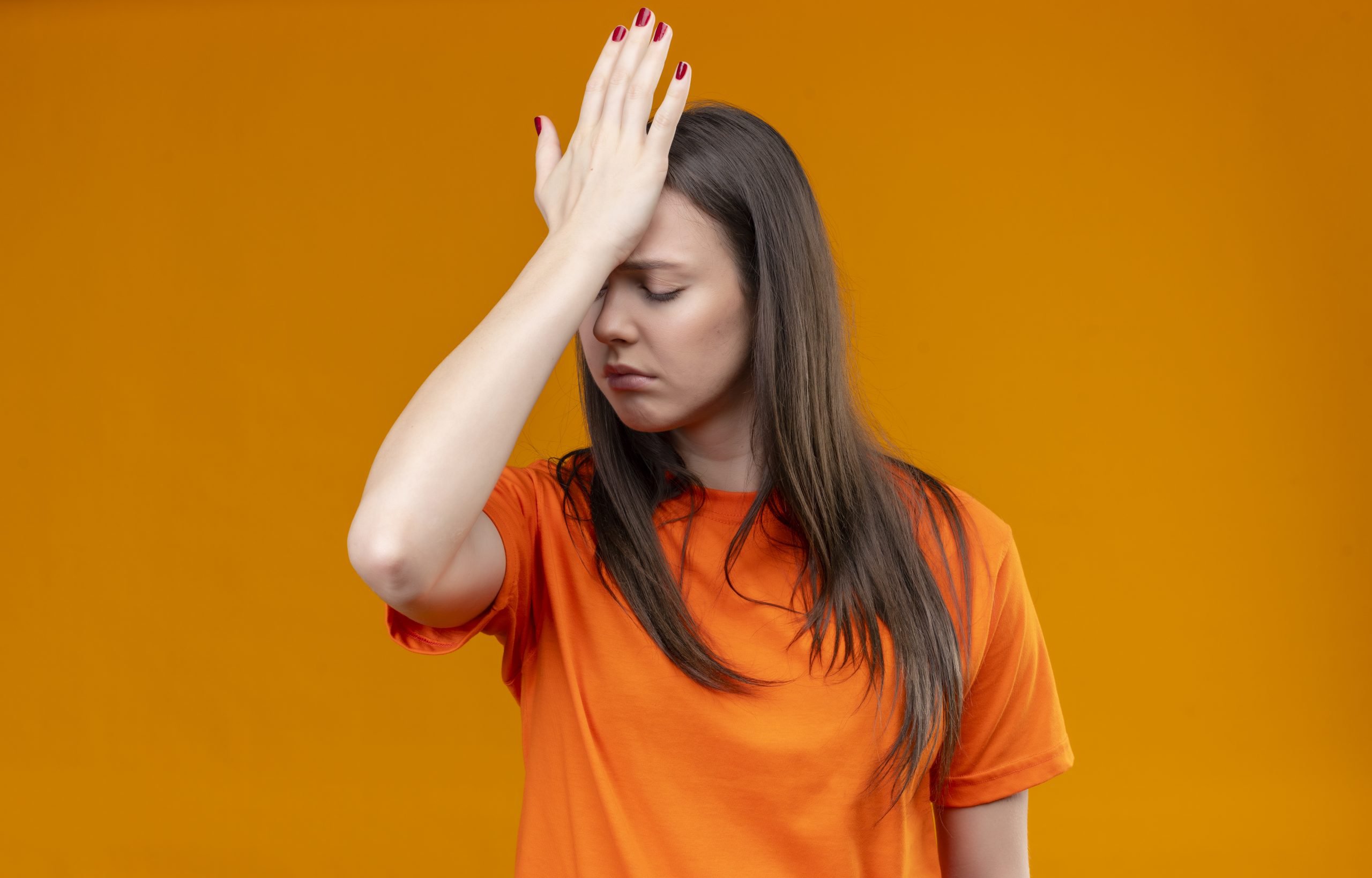 young beautiful girl wearing orange t shirt standing with hand head mistake looking unhappy with sad expression face isolated orange background scaled